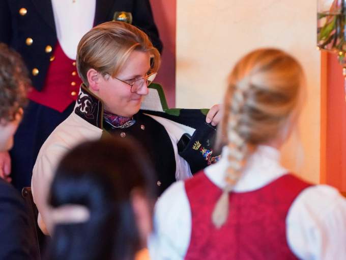 – Jeg må si det er en fryd å se deg i din nye Aust-Telemark-bunad, sa Dronning Sonja i sin tale til jubilanten, som viser fram innerlommen på bunaden som Dronningen har brodert. Foto: Terje Pedersen / NTB