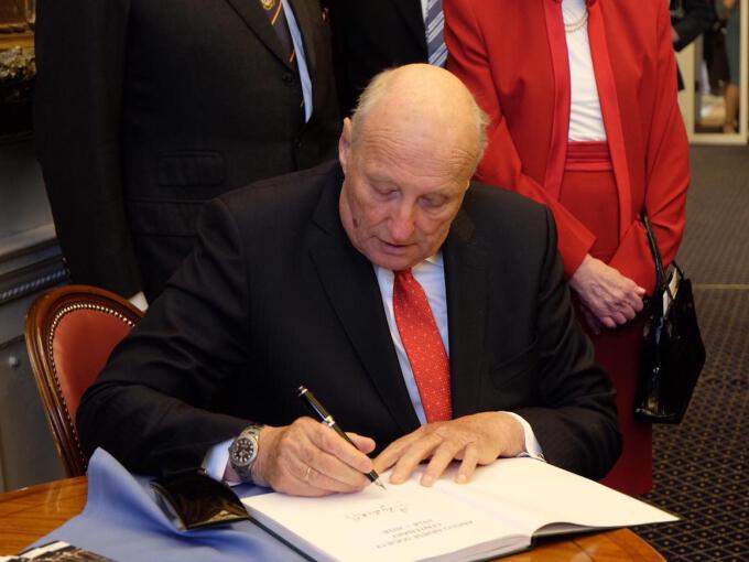 Kong Harald signerer gjesteboken hos the Anglo-Norse Society. Foto: The Royal Court, UK